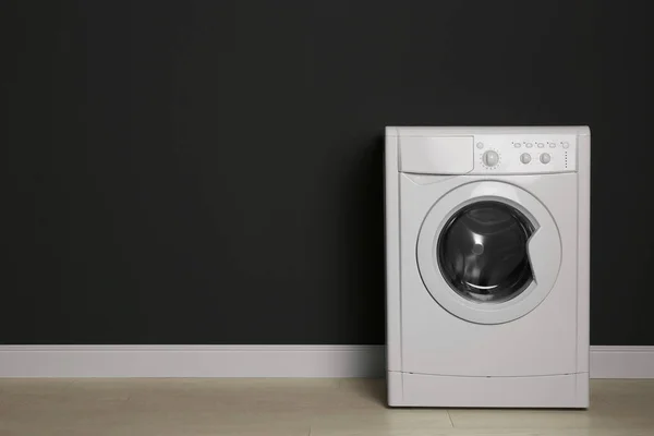 Modern washing machine near black wall, space for text. Laundry — Stock Photo, Image