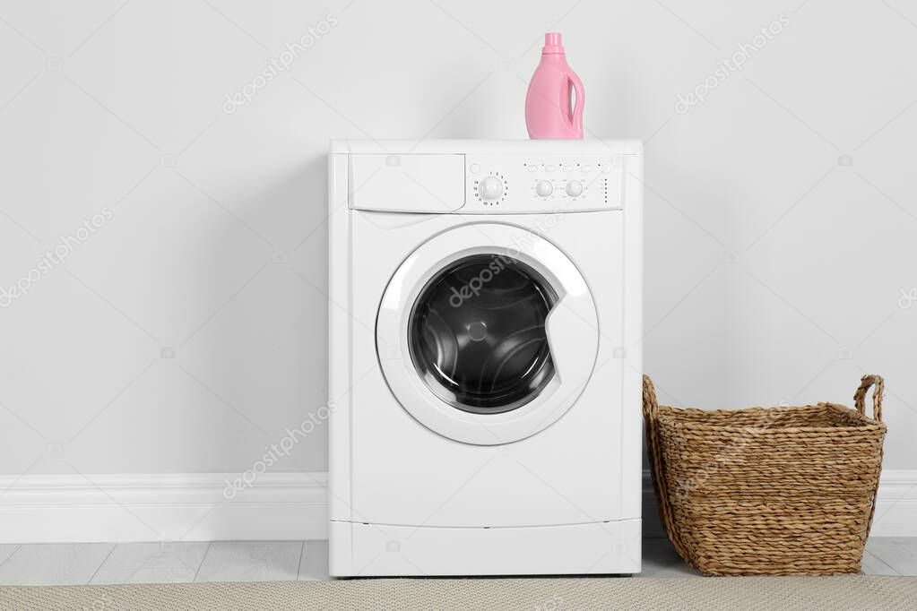 Modern washing machine with detergent and laundry basket near wh