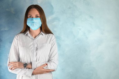 Yüzü açık mavi arka planda tek kullanımlık maskeli bir kadın. Metin için boşluk
