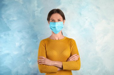 Yüzü açık mavi arka planda tek kullanımlık maskeli kadın