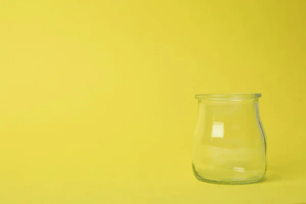 Open empty glass jar on light yellow background, space for text