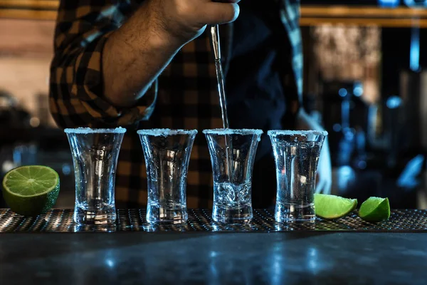 Bartender pouring Mexican Tequila into shot glasses at bar counter, closeup