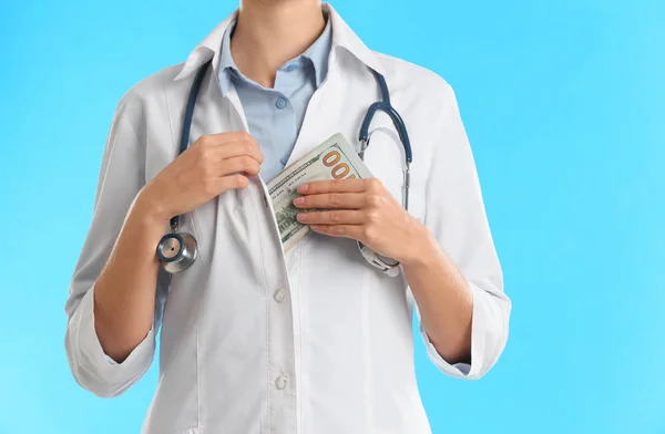 Doctor putting bribe money into pocket on light blue background, — Stock Photo, Image