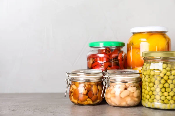 Glasburkar med olika betade grönsaker på grått bord. Spac — Stockfoto