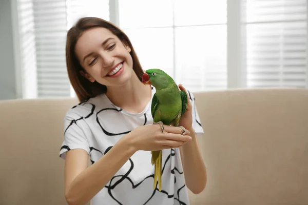 Young woman with cute Alexandrine parakeet indoors — 스톡 사진