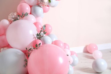 Bej duvarın yanında balonlar ve yeşil yapraklarla güzel bir kompozisyon.