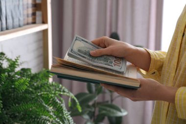 Kitapların içine dolar banknotları saklayan kadın, yakın plan. Para tasarrufu