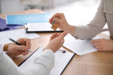 Real estate agent giving key with trinket to client in office, closeup