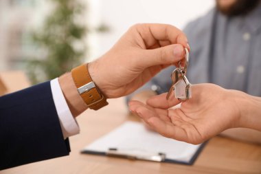 Real estate agent giving key with trinket to client in office, c