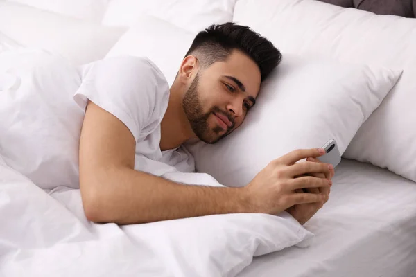 Молодой человек, зависимый от смартфона в постели дома — стоковое фото