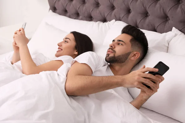Jovem casal com smartphones na cama em casa — Fotografia de Stock