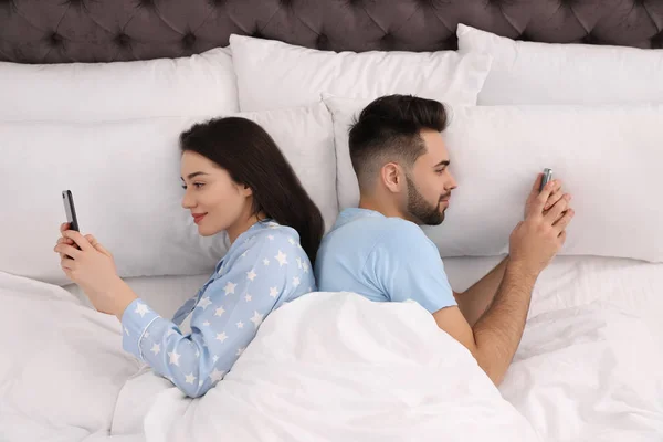 Pareja joven adicta a los teléfonos inteligentes en la cama en casa, vista superior — Foto de Stock