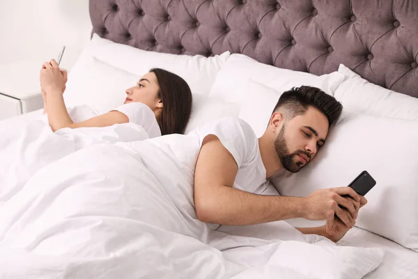 Pareja joven adicta a los teléfonos inteligentes en la cama en casa — Foto de Stock