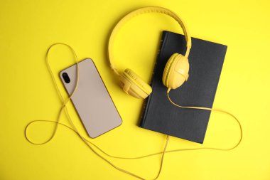 Book, modern headphones and smartphone on yellow background, fla