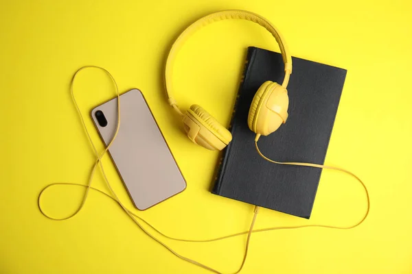 Livro, fones de ouvido modernos e smartphone em fundo amarelo, fla — Fotografia de Stock