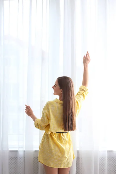 Νεαρή γυναίκα κοντά στο παράθυρο με κουρτίνες σε εσωτερικούς χώρους — Φωτογραφία Αρχείου