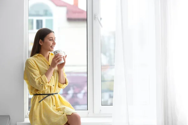 Giovane donna con coppa sul davanzale della finestra al chiuso — Foto Stock