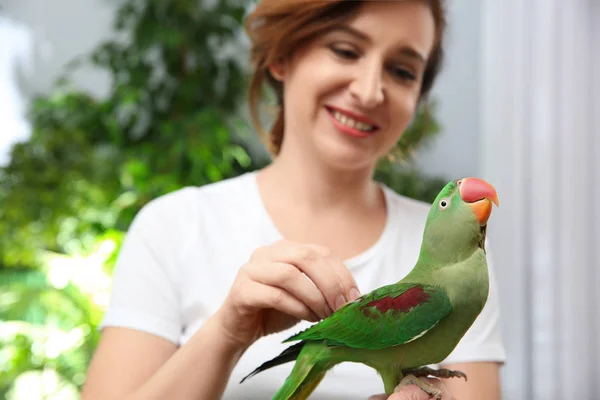 Happy woman with Alexandrine parakeet on blurred background — 스톡 사진