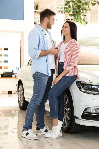 Happy couple with car key in modern auto dealership