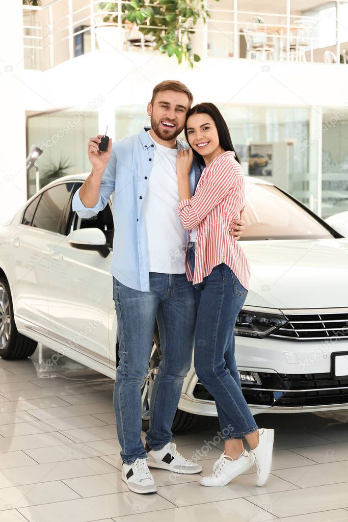 Happy couple with car key in modern auto dealership