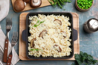 Açık mavi ahşap masada peynirli ve mantarlı leziz risotto.