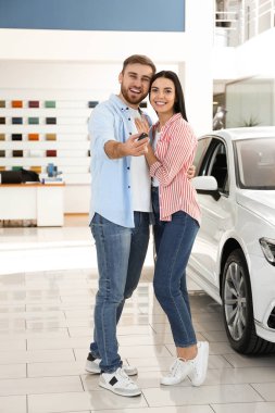 Modern oto galerisinde araba anahtarı olan mutlu bir çift.