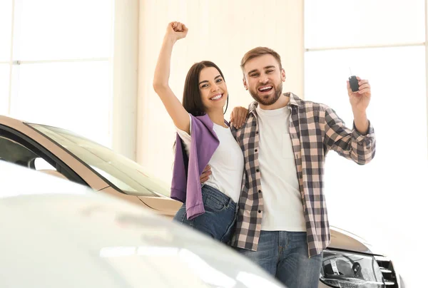 Happy couple with car key in modern auto dealership