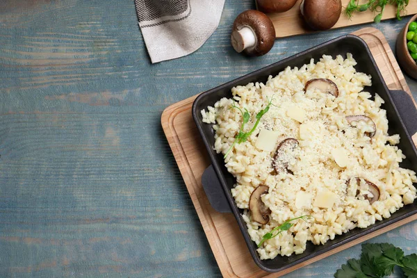 Delicious risotto with cheese and mushrooms on light blue wooden table, flat lay. Space for text