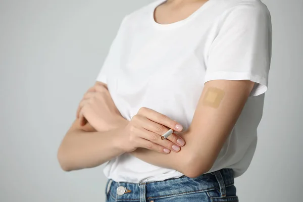 Young woman with nicotine patch and cigarette on light grey back — Stock Photo, Image