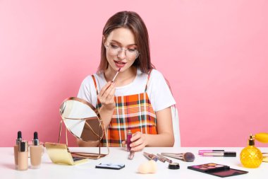 Güzellik blogcusu pembe arka planda ruj sürüyor