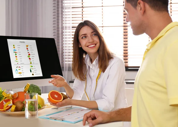 Young nutritionist consulting patient at table in clinic — Stock Photo, Image