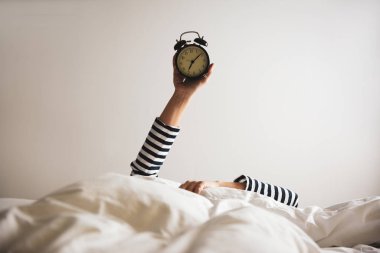 Çalar saati olan kadın yatakta yatıyor, yakın plan. Sabah oldu.