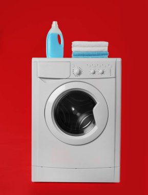 Havlu yığını ve kırmızı üzerine deterjan yığılmış modern çamaşır makinesi.