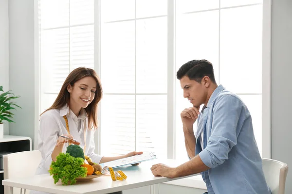 Joven nutricionista consultando al paciente en la mesa de la clínica —  Fotos de Stock