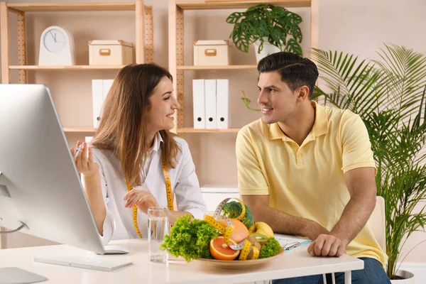 Young nutritionist consulting patient at table in clinic — Stock Photo, Image