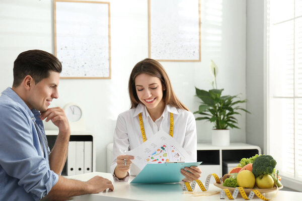 Young nutritionist consulting patient at table in clinic