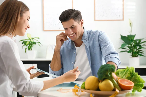 Young nutritionist consulting patient at table in clinic — Stock Photo, Image