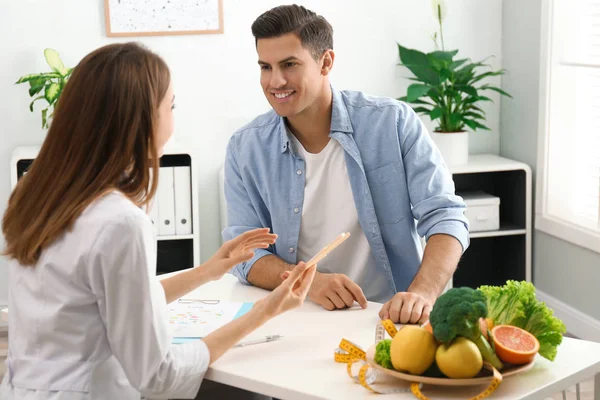 Young nutritionist consulting patient at table in clinic — Stock Photo, Image