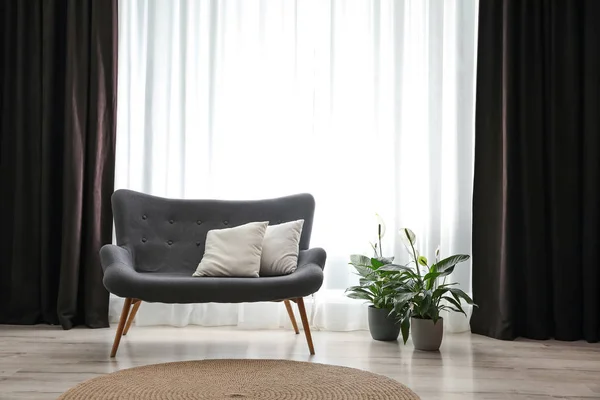 Cómodo sofá cerca de la ventana con elegantes cortinas en la habitación —  Fotos de Stock