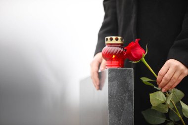 Woman holding red rose near black granite tombstone with candle 