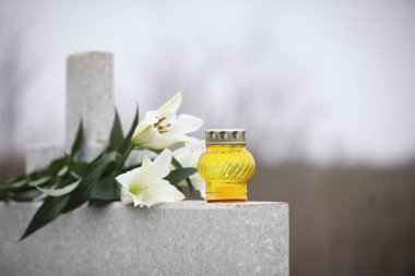 Açık havada açık gri granit mezar taşı üzerinde beyaz zambaklar ve mum.