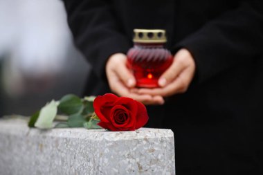 Woman holding candle near grey granite tombstone outdoors, close