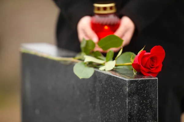 Woman with candle near black granite tombstone outdoors, focus o — 스톡 사진