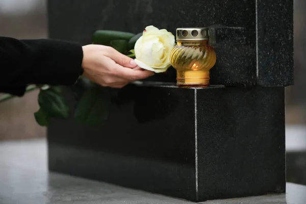 Mulher segurando rosa branca perto de pedra tumular de granito preto com vela — Fotografia de Stock