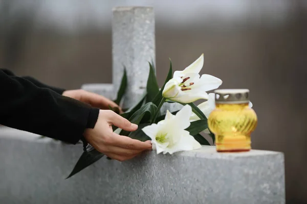 Woman holding white lilies near light grey granite tombstone wit — 스톡 사진