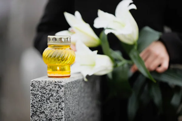 Woman holding white lilies near grey granite tombstone outdoors, — Stock Photo, Image