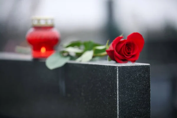 Rote Rose und Kerze auf schwarzem Granitgrabstein im Freien. Beerdigung — Stockfoto