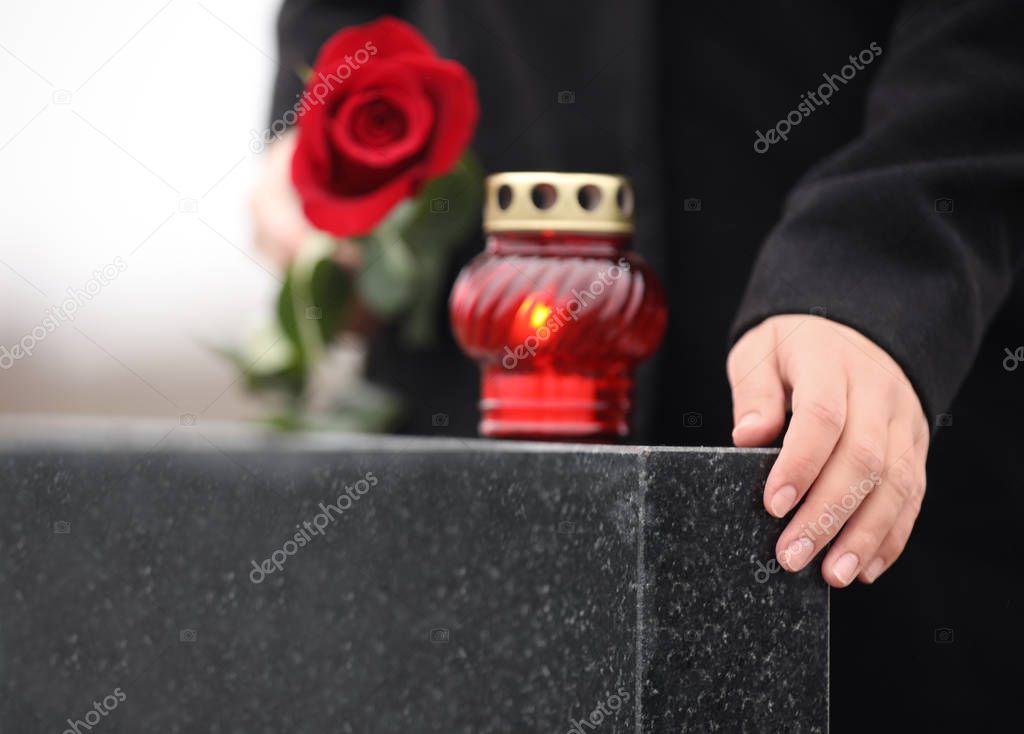 Woman holding red rose near black granite tombstone with candle 