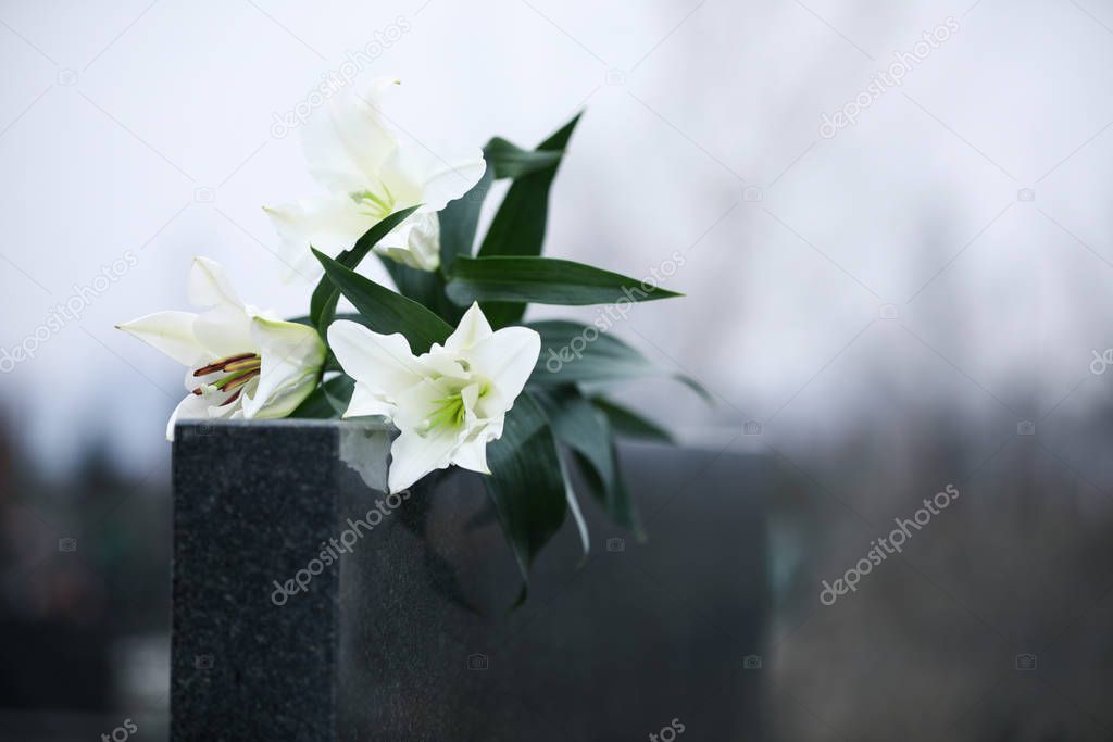 White lilies on black granite tombstone outdoors, space for text