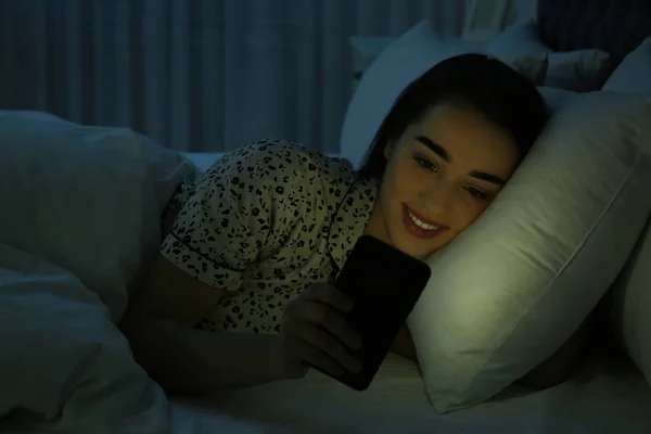 Mladá žena závislá na smartphone v posteli v noci — Stock fotografie